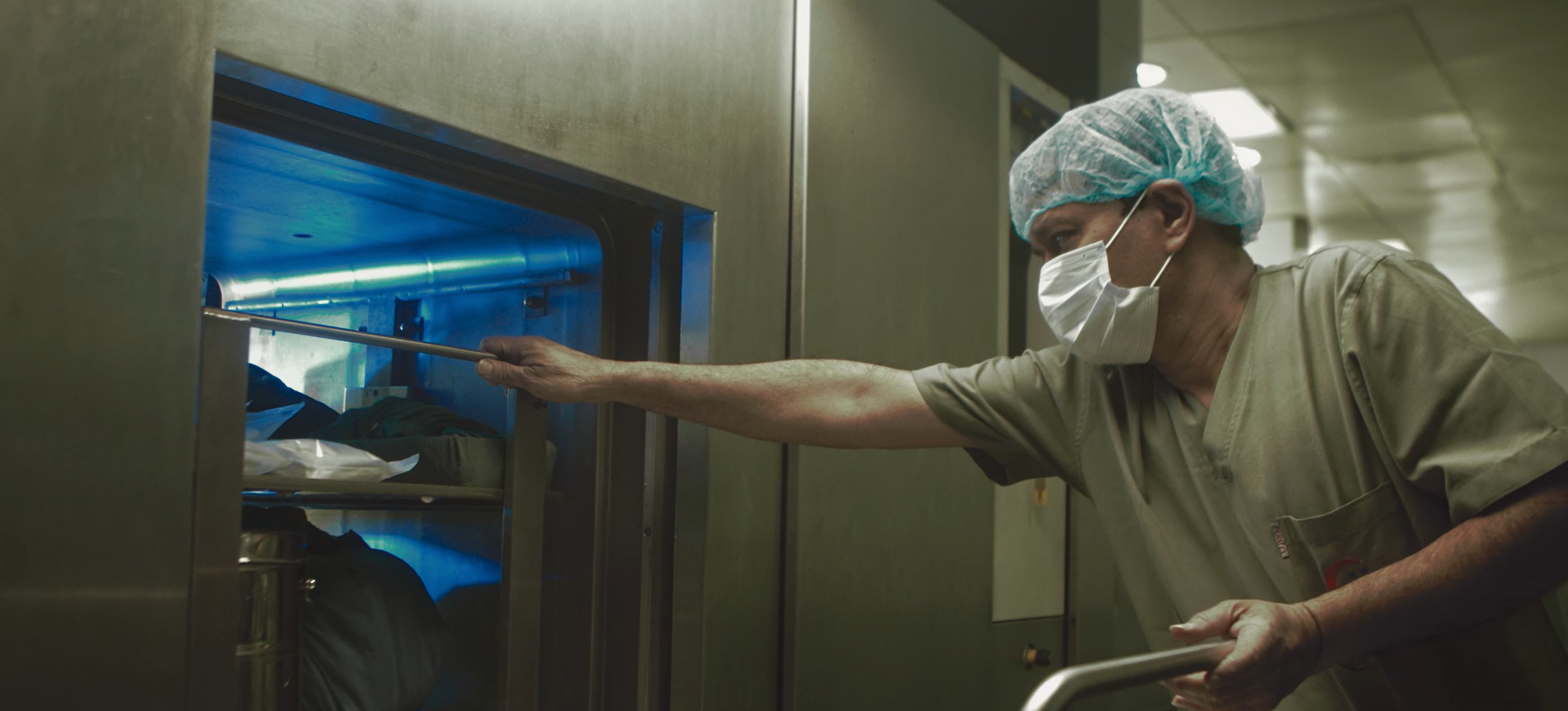A masked hospital worker handling a tray inside blue-lit equipment