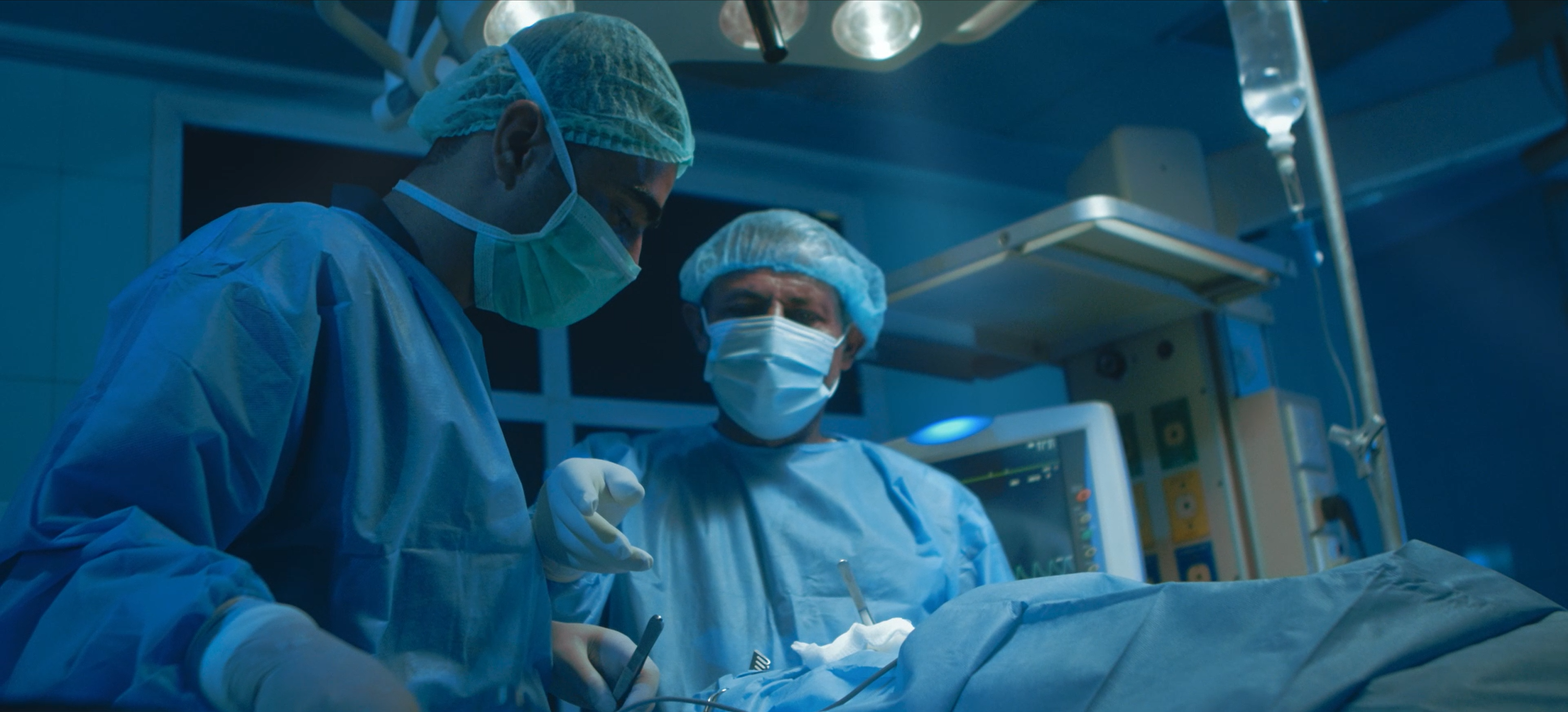 Two masked surgeons working under blue operating-room light